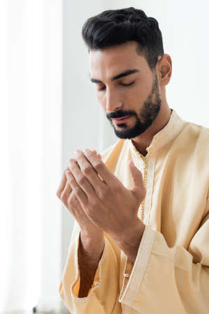 Young arabian man closing eyes while praying at home