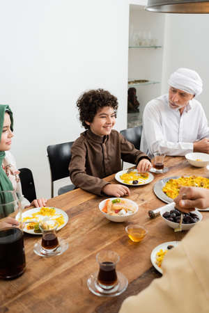 happy multiethnic kids having dinner near muslim grandfather at homeの写真素材