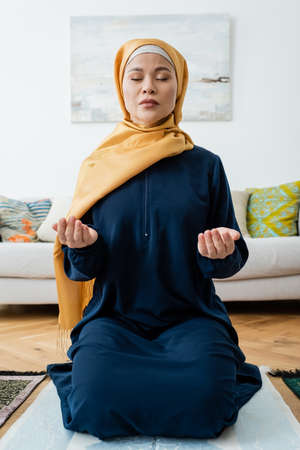 Asian woman praying with closed eyes on traditional rug at homeの写真素材