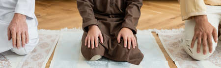 Cropped view of arabian kid sitting on rug near family at home, bannerの写真素材