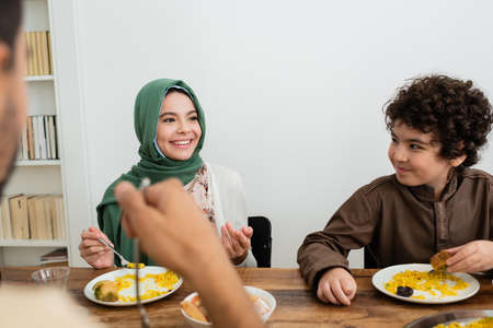 smiling muslim girl pointing with finger during dinner with dad and arabian brotherの写真素材