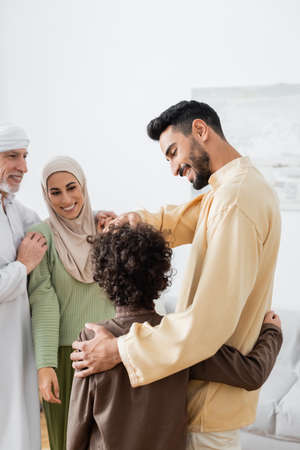 arabian father and son embracing near happy interracial muslim familyの写真素材