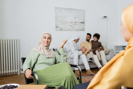 happy muslim woman talking to mother near multiethnic family in living room
