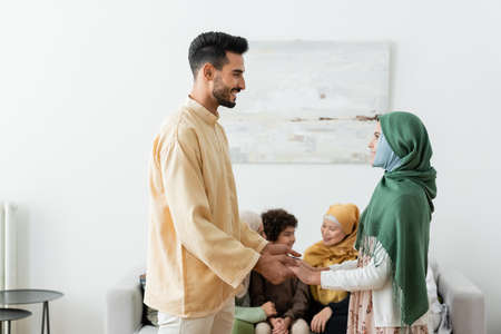 happy arabian man holding hands with daughter near multiethnic muslim family on blurred backgroundの写真素材