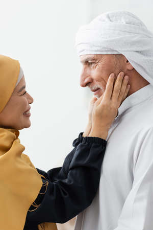 side view of pleased asian woman in hijab touching face of muslim husband