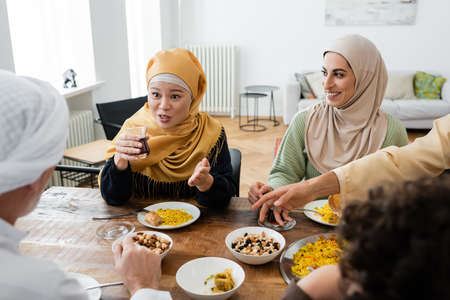 asian woman pointing with hand while talking near smiling muslim daughter and blurred familyの写真素材