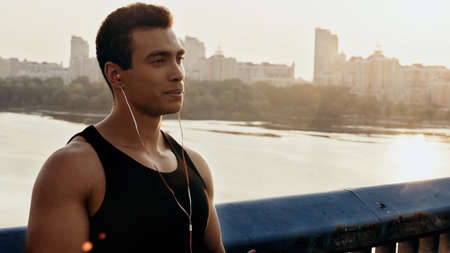 young and athletic mixed race man listening music on bridge over riverの写真素材