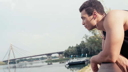 side view of sportive bi-racial man listening music while looking at river