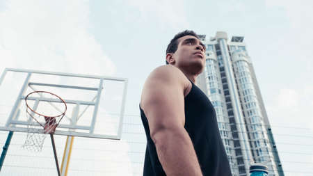 low angle view of athletic mixed race man looking away near basketball ring outdoorsの写真素材