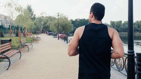 back view of bi-racial athletic man in earphones running on embankment in city