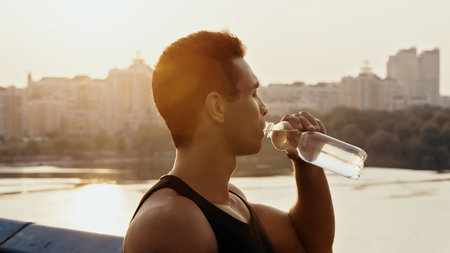 athletic mixed race man drinking water over river in cityの写真素材