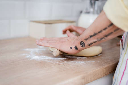 Cropped view of tattooed mature man rolling dough with pin in kitchenの写真素材