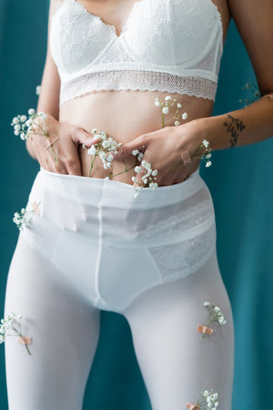 partial view of sexy woman in bra and white tights, with tiny flowers on body, posing on turquoise...