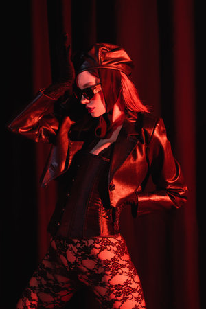 sexy woman in lace leggings, black leather jacket and sunglasses posing with hand on hip on dark...