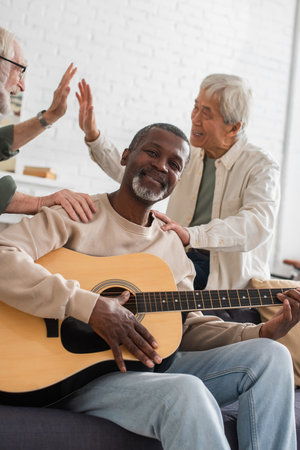 African american man playing acoustic guitar near interracial friends at homeの写真素材