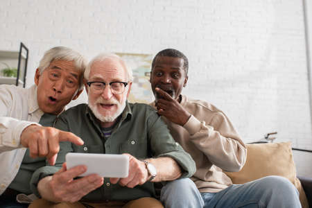 Shocked interracial men looking at smartphone near friend at homeの写真素材