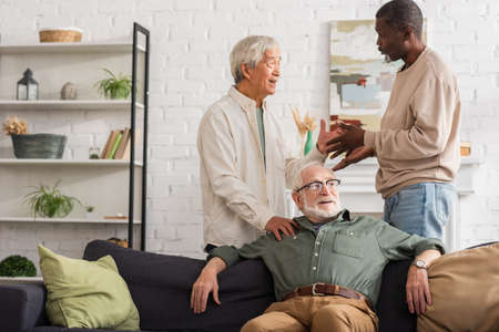 Multiethnic men talking near senior friend on couch at home