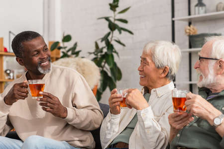 Positive african american man holding tea near multiethnic friends at home