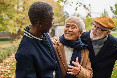 Cheerful asian man talking to multiethnic friends in autumn parkの写真素材