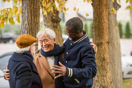Happy asian man hugging senior interracial friends on urban streetの写真素材