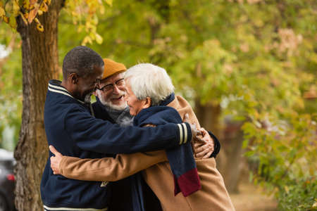 Positive multicultural friends hugging in autumn park