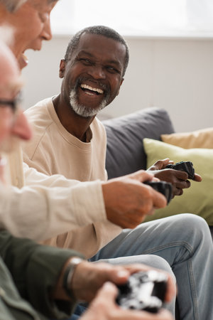 KYIV, UKRAINE - OCTOBER 12, 2021: Cheerful african american man playing video game with senior...
