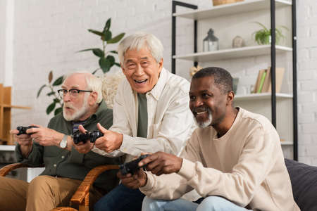 KYIV, UKRAINE - OCTOBER 12, 2021: Smiling asian man looking at camera while playing video game near...
