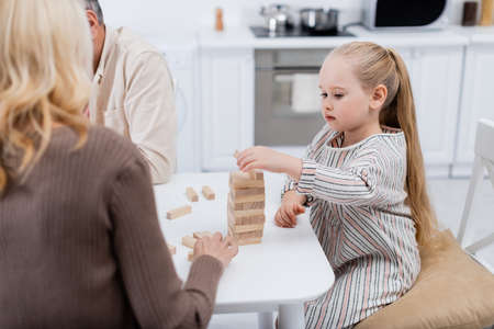 girl playing wood blocks game near blurred grandparents in kitchenの写真素材