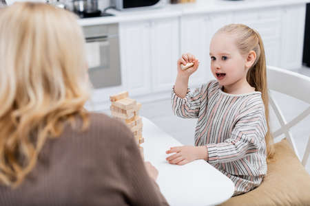 amazed girl playing wood blocks game near blurred granny in kitchenの写真素材