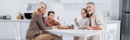 happy kids with grandparents looking at camera while playing chess in kitchen, bannerの写真素材