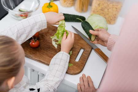 top view of cropped granny and granddaughter near fresh vegetables and chopping boardの写真素材