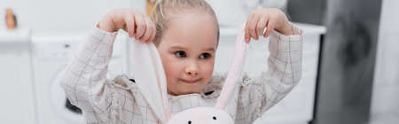 little girl playing with toy bunny in kitchen, banner