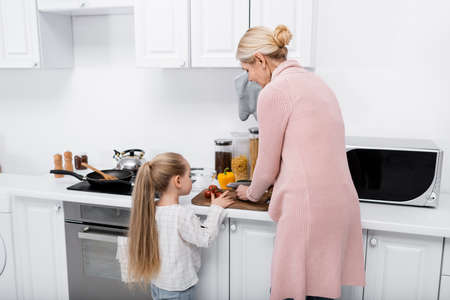 middle aged woman cutting vegetables near granddaughter in kitchenの写真素材