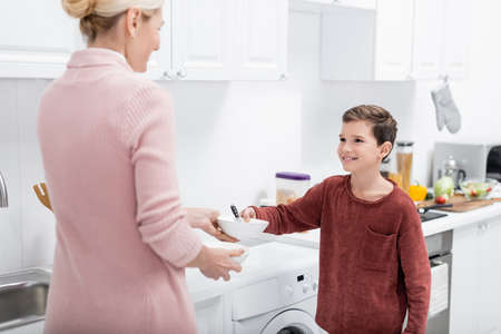 smiling boy giving bowl to grandmother while helping her in kitchen