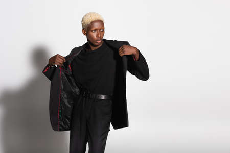 trendy african american man with bleached hair undressing on gray with shadow