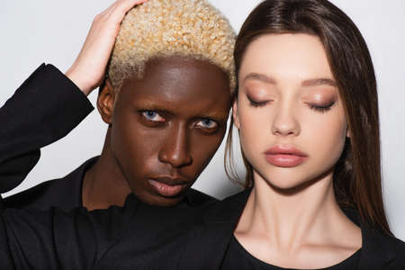 pretty brunette woman with closed eyes touching hair of blonde african american man on gray