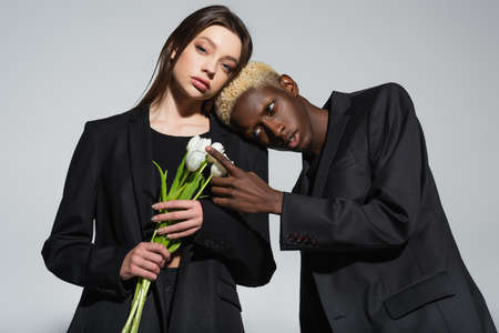 stylish african american man with bleached hair touching white tulips near young brunette woman...