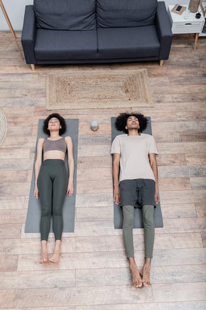 Top view of african american couple lying on yoga mats in living roomの写真素材