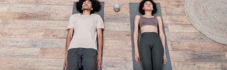 Top view of african american couple lying on yoga mats at home, bannerの写真素材