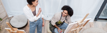 Overhead view of african american man painting on canvas near girlfriend at home, bannerの写真素材