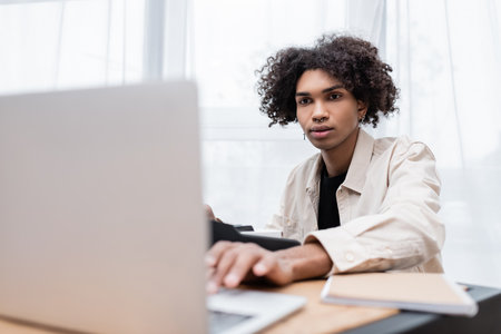 Young african american man using laptop and playing synthesizer at home