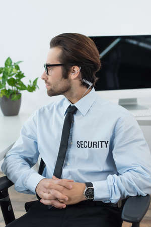 security man in earphone and eyeglasses sitting with clasped hands and looking awayの写真素材
