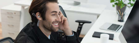 cheerful security man in earphone looking at blurred computer monitor, banner