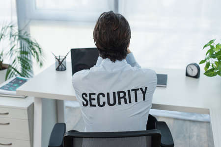 back view of guard in shirt with security lettering sitting near laptop in office