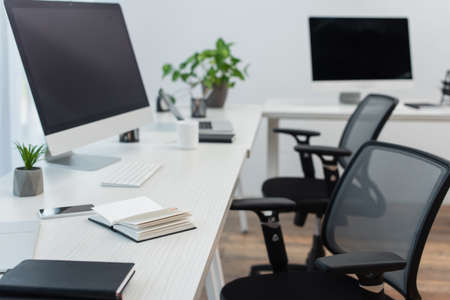desks with computer monitors, blurred laptop and notebooks near office chairsの写真素材