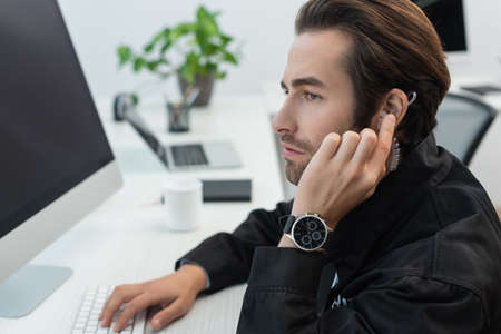 serious security man touching earphone while working in supervision room