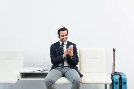 happy traveler using smartphone while listening to music in headphones in departure loungeの写真素材