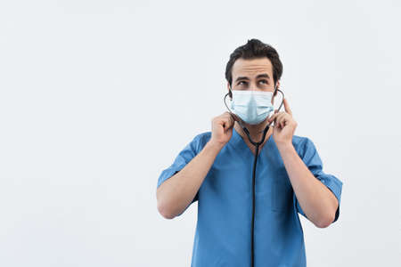 thoughtful physician in medical mask using stethoscope isolated on grayの写真素材