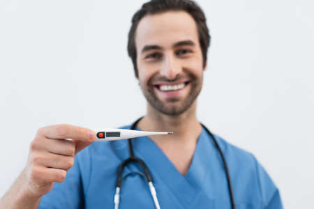 blurred doctor with electronic thermometer smiling on blurred background isolated on gray