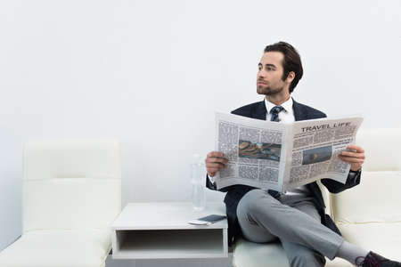 man with travel life newspaper looking away while sitting in departure lounge